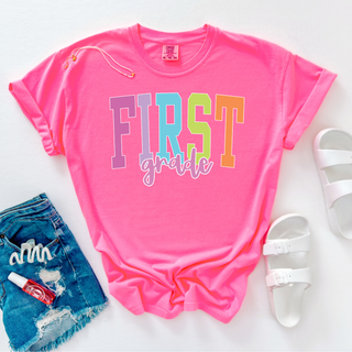 Neon pink First Grade rainbow letter graphic shirt styled with denim shorts and white sandals