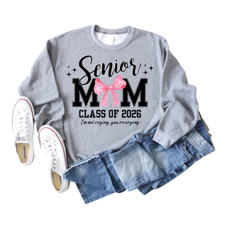 Senior Mom Class of 2026 Graphic Crewneck in gray with black and pink text and bow, includes phrase I’m not crying, you’re crying, displayed flat with jeans and white sneakers.