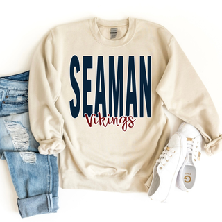 Front view of Seaman Vikings Stacked Script Graphic Top on sand color with navy text, styled with folded sleeves, paired with light-wash jeans and white sneakers, showcasing a casual team apparel look.