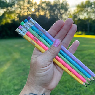 Hand holding personalized pastel #2 wooden pencils with custom laser engraved names in soft pink, yellow, green, and blue colors for back to school supplies and classroom organization