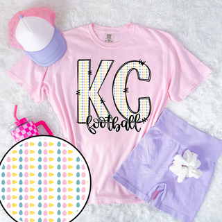 Pink Comfort Colors KC Football shirt featuring pastel egg pattern letters with stitched outline graphic styled with lilac shorts and accessories.