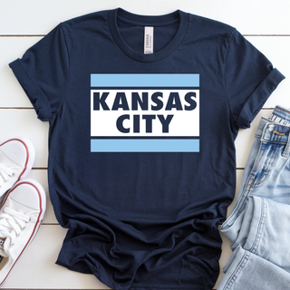Kansas City stripe block graphic top featuring bold blue horizontal bars and layered city lettering on a navy unisex style tee