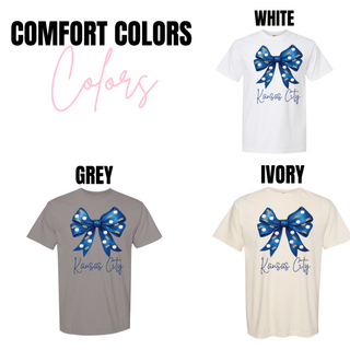 Kansas City baseball bow graphic Comfort Colors short sleeve tops shown in white, grey, and ivory featuring a blue bow with crown and baseball pattern and Kansas City script text.