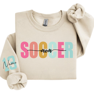 Soccer Mom personalized sweatshirt with blue print lettering and custom sleeve number, shown on a sand crewneck.