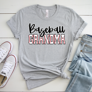Baseball Grandma graphic displayed on a light grey top featuring bold black script lettering layered over varsity block text filled with red baseball seam detailing, styled in a flat lay with rolled sleeves and paired with denim and white sneakers.