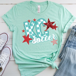 Heather Prism Mint Bella Canvas top featuring a KC soccer graphic with teal checkerboard KC lettering, bold red star accents, and white script soccer text layered across the front in a vibrant Kansas City inspired design.