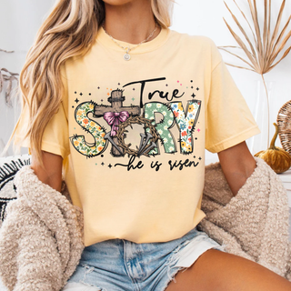 True Story He Is Risen Christian graphic top featuring floral patterned letters, rustic wooden cross, crown of thorns, and pink bow detail on a soft yellow unisex style