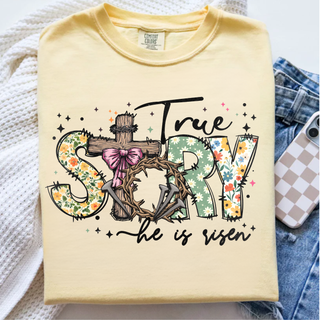 True Story He Is Risen Christian graphic top featuring floral patterned letters, rustic wooden cross, crown of thorns, and pink bow detail on a soft yellow unisex style
