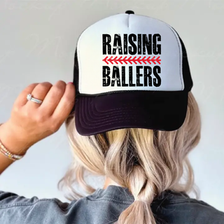 Raising Ballers black and white foam trucker hat with distressed black lettering and red arrow detail on front panel worn by woman with blonde braid
