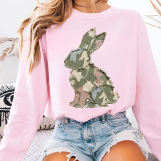 Woman wearing a light pink crewneck sweatshirt with a camouflage patchwork bunny graphic on the front.