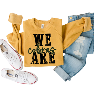 Jackson Heights We Are Cobras crewneck in mustard, flat lay with jeans
