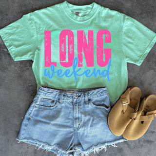 long weekend graphic shirt on chalky mint comfort colors tee with pink distressed lettering and blue script text styled with denim shorts