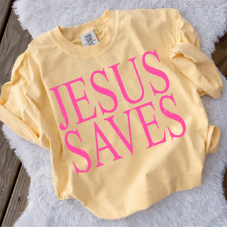 Jesus Saves bold pink graphic printed on butter yellow Comfort Colors top laid flat on soft background