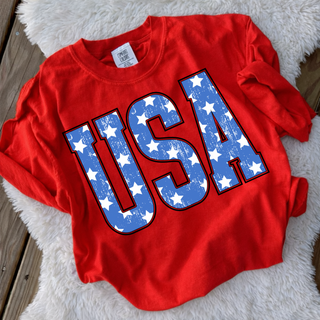 distressed USA stars graphic in blue with white stars on red shirt styled flat lay on wood background with neutral blanket