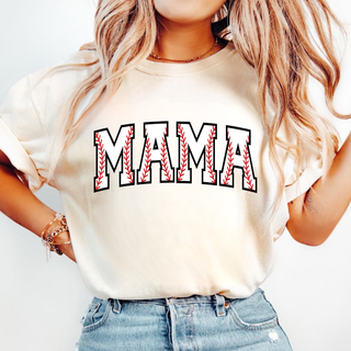 Woman wearing an ivory graphic top with bold varsity-style MAMA lettering featuring red baseball stitch detail inside each letter and a black outline, styled with light wash denim shorts