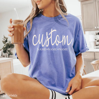 personalized custom name graphic tee in periwinkle blue with script text and multiple names underneath styled casually with iced coffee