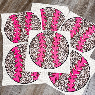 Leopard print softball graphic transfers with bright pink stitching arranged on surface