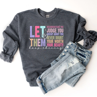  Let Them Keep Shining Top in Dark Heather Grey Gildan crewneck sweatshirt with colorful motivational Let Them graphic and keep shining script lettering, flat lay styled with distressed denim jeans and grey scrunchie