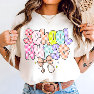 Woman wearing Retro Checkered School Nurse Graphic Top in ivory with multicolor checkered School Nurse lettering bow and stethoscope design
