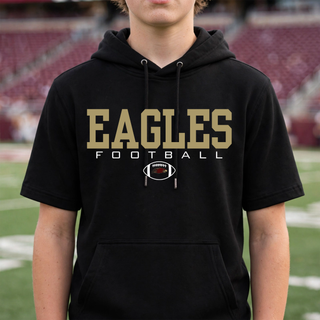 Model wearing the Silver Lake Eagles Football Standard Short Sleeve Hooded Pullover in black at a football stadium.
