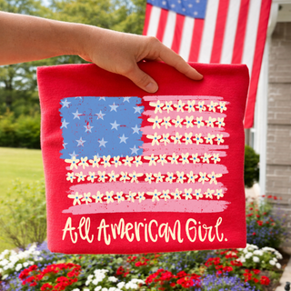 Red crewneck held up outdoors with floral American flag and All American Girl script design