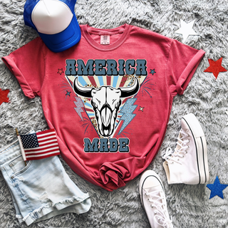 Crimson Comfort Colors tee with America Made bull skull graphic featuring a western bull skull with leopard print lightning bolts, sunburst background, and bold America Made lettering with stars
