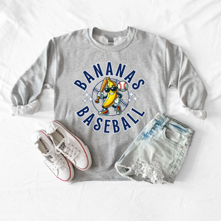 Sport grey crewneck with cartoon banana mascot in sunglasses holding baseball bat in circular design styled flat lay with sneakers and denim shorts
