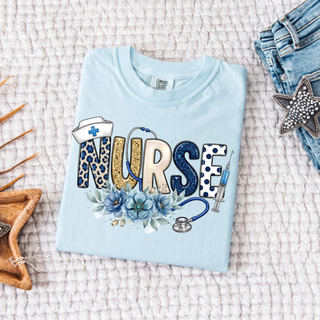 Blue Floral Nurse Graphic Top in chambray with mixed print Nurse lettering nurse hat stethoscope syringe and blue floral design

