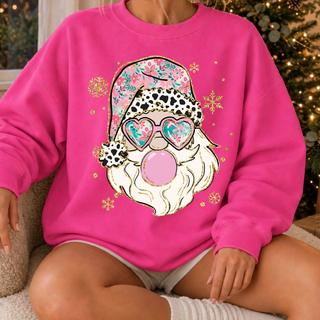 Model wearing a hot pink crewneck sweatshirt with a bubblegum Santa graphic featuring a floral hat, cow print trim, heart sunglasses, and gold glitter snowflakes