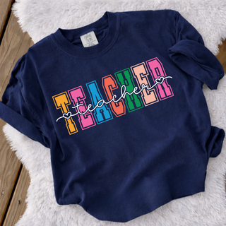 Colorful varsity teacher script graphic on a navy Comfort Colors short sleeve tee, flat lay
