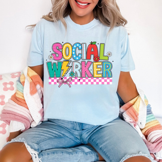 Woman wearing light blue checkered social worker top with colorful lettering and pink bow
