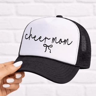Black and white trucker hat with script cheer mom and bow, held in hand