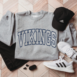 Sport grey Gildan crewneck with vikings varsity arch outline graphic, flat lay with hat and sneakers
