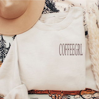 White crewneck with brown Coffeegrl left chest text styled with a tan hat and fall blanket
