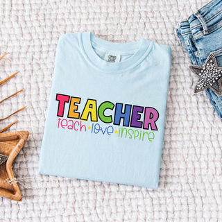 Chambray Comfort Colors tee folded flat with colorful TEACHER teach love inspire block letter design
