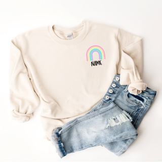 Sand Gildan crewneck with pastel rainbow and custom name text left chest pocket design front view
