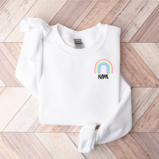 White Gildan crewneck with pastel rainbow and custom name text left chest pocket design flat lay