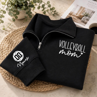 Black quarter-zip styled flat lay with VOLLEYBALL mom lettering on the chest and a volleyball graphic with custom number and name on the sleeve