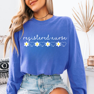 Woman wearing flo blue Comfort Colors Daisy Registered Nurse Graphic Top long sleeve with white script and daisy stethoscope heart row design
