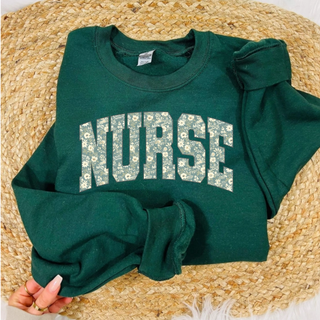 Forest green crewneck held flat with floral NURSE varsity arch letter design in cream and green
