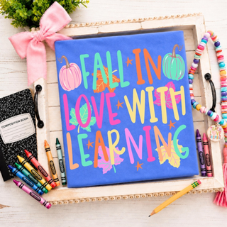 Fall In Love With Learning graphic tee in flo blue with pumpkins, leaves, and colorful lettering on styled tray