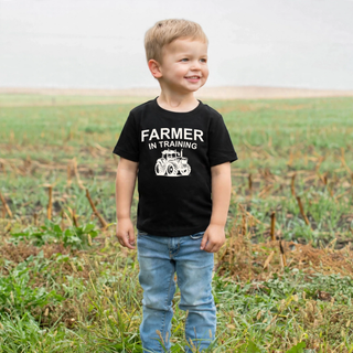 Toddler wearing black farmer in training top with tractor graphic in a field