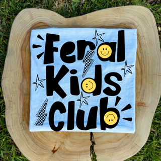 Light blue Feral Kids Club top with checkered lightning bolts and smiley faces flat lay on wood stump
