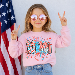 Young girl in pink crewneck with firecracker doodle mini patriotic graphic, pink sunglasses, American flag background
