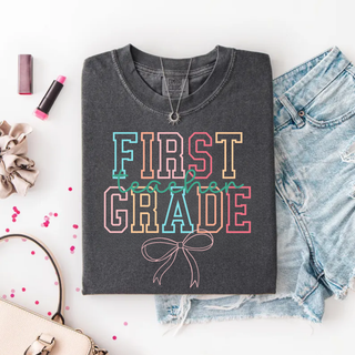 First grade teacher graphic tee in pepper with colorful bow design folded with lipstick and denim
