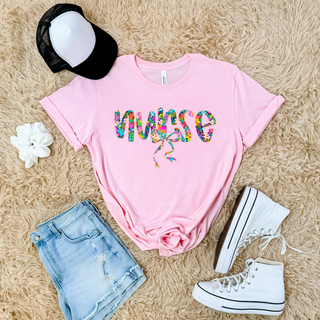 Bella Canvas pink short sleeve top laid flat with colorful floral nurse script and bow graphic styled with denim shorts and white high top sneakers