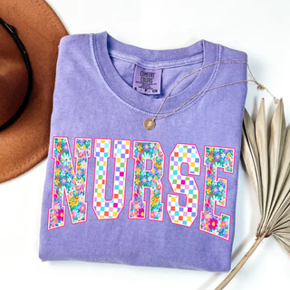 Floral Checkered Nurse Graphic Top in violet with colorful floral and rainbow checkered NURSE block letter design

