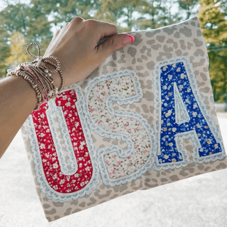 Hand holding leopard print tee with floral USA letters in red white and blue with lace border detail
