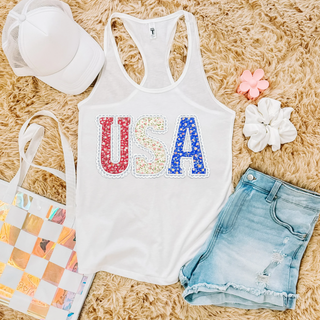 White racerback tank flat lay with floral USA letters in red white and blue with lace border detail
