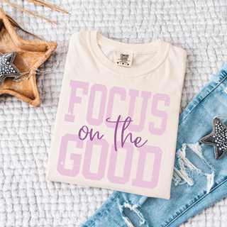 Folded ivory Comfort Colors tee with distressed lavender Focus on the Good varsity graphic
